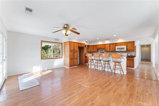 kitchen with tasteful backsplash, a kitchen breakfast bar, a center island, ceiling fan, and light wood-type flooring