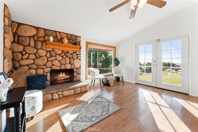 living area with ceiling fan, a fireplace, light hardwood / wood-style floors, vaulted ceiling, and french doors