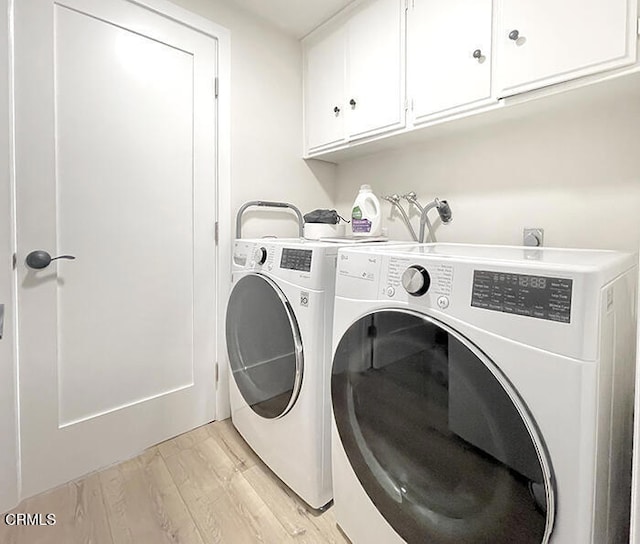 laundry area featuring cabinets, washing machine and clothes dryer, and light hardwood / wood-style floors