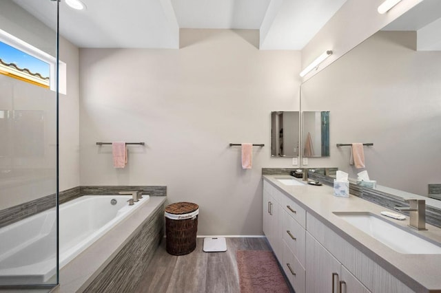 bathroom with hardwood / wood-style floors, vanity, and a relaxing tiled tub