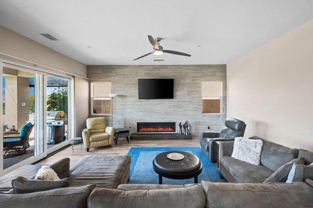 living room featuring a tile fireplace, ceiling fan, and light wood-type flooring