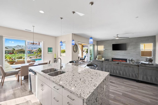 kitchen with sink, white cabinetry, light stone countertops, a center island with sink, and decorative light fixtures