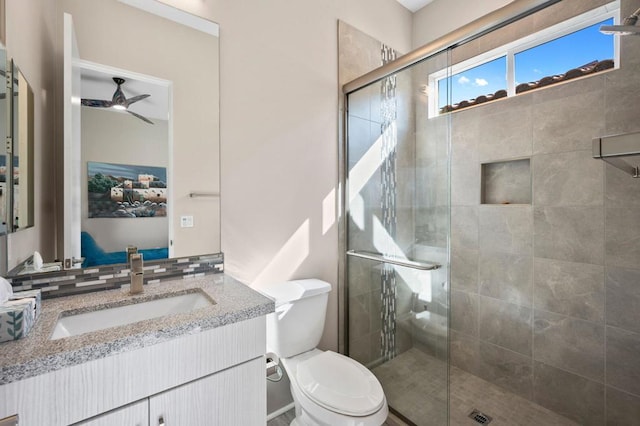 bathroom featuring a shower with shower door, decorative backsplash, vanity, ceiling fan, and toilet