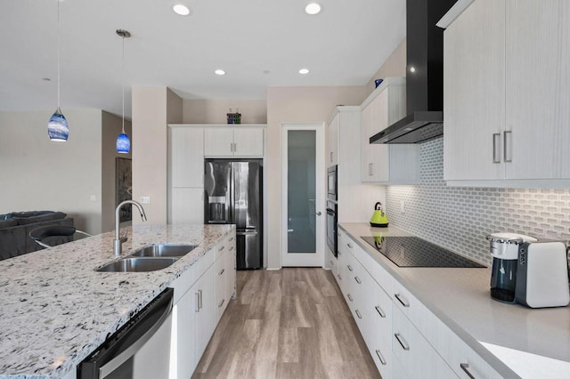 kitchen with decorative light fixtures, sink, white cabinets, black appliances, and wall chimney range hood