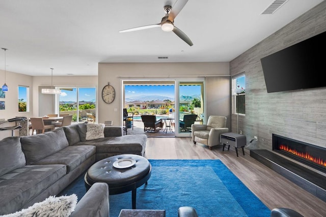 living room featuring a wealth of natural light, a fireplace, ceiling fan, and light wood-type flooring