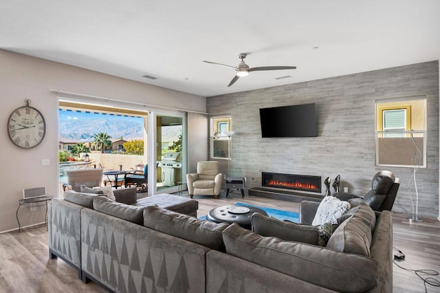 living room with a tiled fireplace, ceiling fan, and light wood-type flooring