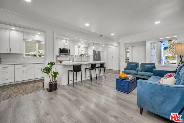 living room featuring crown molding, a healthy amount of sunlight, and light wood-type flooring