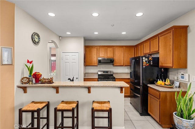 kitchen with a breakfast bar, light stone counters, black appliances, light tile patterned flooring, and kitchen peninsula