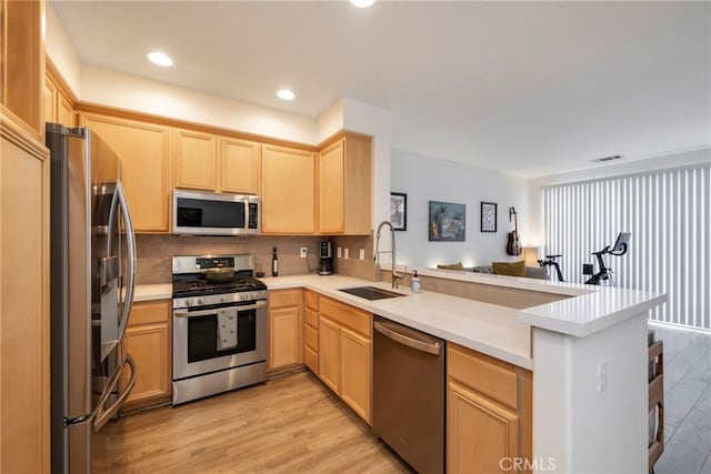 kitchen with appliances with stainless steel finishes, kitchen peninsula, sink, and light brown cabinets