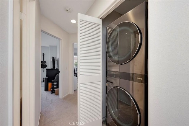 laundry room featuring stacked washer / drying machine and light colored carpet