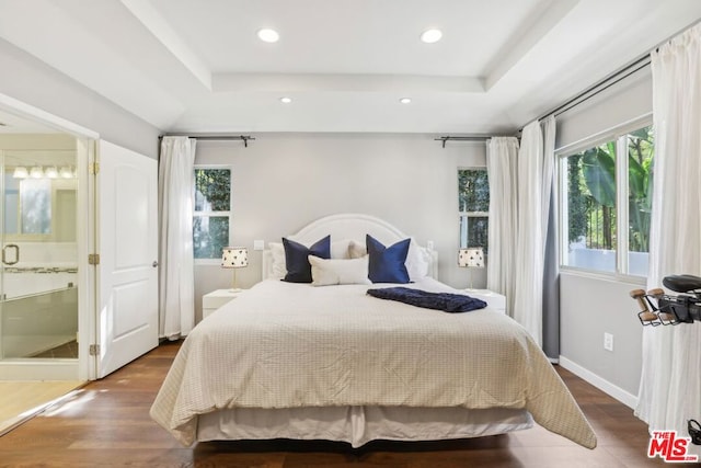 bedroom featuring a raised ceiling, ensuite bathroom, and hardwood / wood-style floors