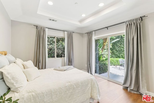 bedroom with multiple windows, a tray ceiling, access to outside, and wood-type flooring