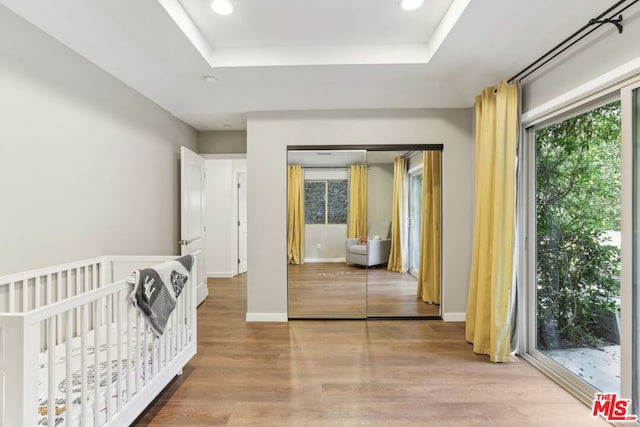 bedroom with a closet, a tray ceiling, light hardwood / wood-style floors, and a nursery area