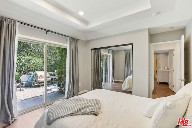 bedroom featuring wood-type flooring, access to exterior, and a tray ceiling