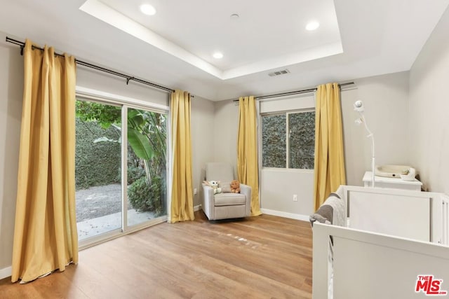 bedroom with access to exterior, a tray ceiling, and light hardwood / wood-style flooring