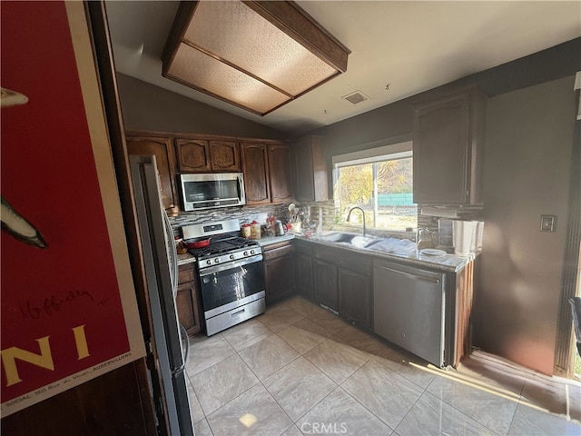 kitchen featuring sink, vaulted ceiling, light tile patterned floors, stainless steel appliances, and decorative backsplash