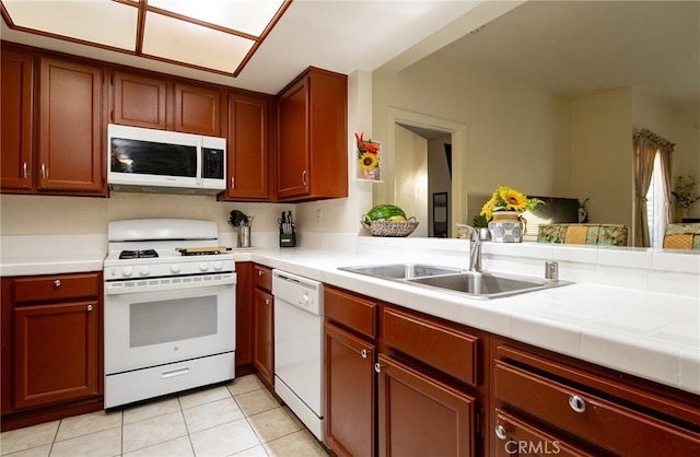 kitchen with sink, tile countertops, light tile patterned floors, kitchen peninsula, and white appliances