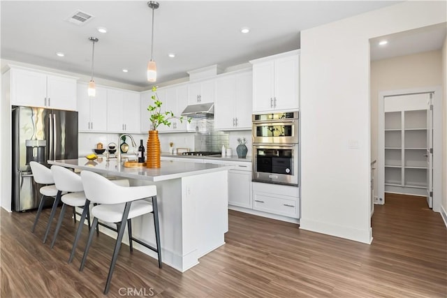 kitchen with stainless steel appliances, pendant lighting, a center island with sink, and white cabinets