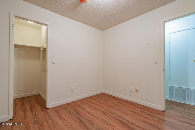 unfurnished bedroom featuring a closet, a spacious closet, light hardwood / wood-style floors, and a textured ceiling