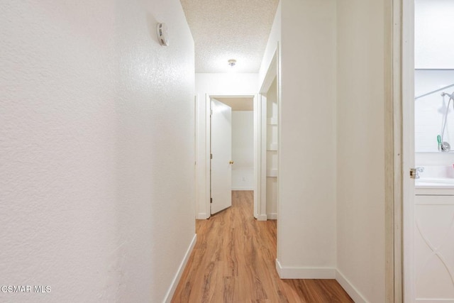 corridor with washer / dryer, light hardwood / wood-style flooring, and a textured ceiling