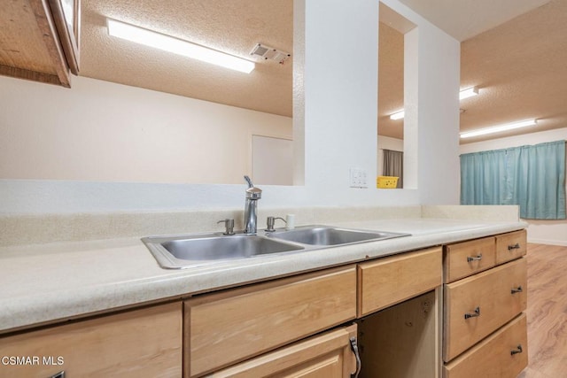 kitchen with light brown cabinetry, sink, a textured ceiling, and light wood-type flooring