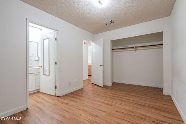 unfurnished bedroom with a closet, ensuite bathroom, a textured ceiling, and light hardwood / wood-style flooring