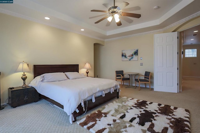 carpeted bedroom with a tray ceiling, ornamental molding, and ceiling fan