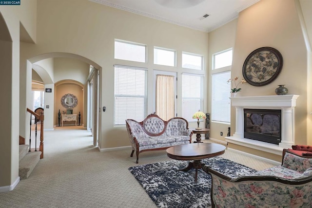 living room featuring a towering ceiling, ornamental molding, and light carpet