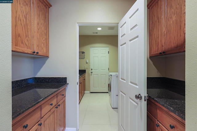 kitchen featuring washing machine and dryer, light tile patterned flooring, and dark stone counters