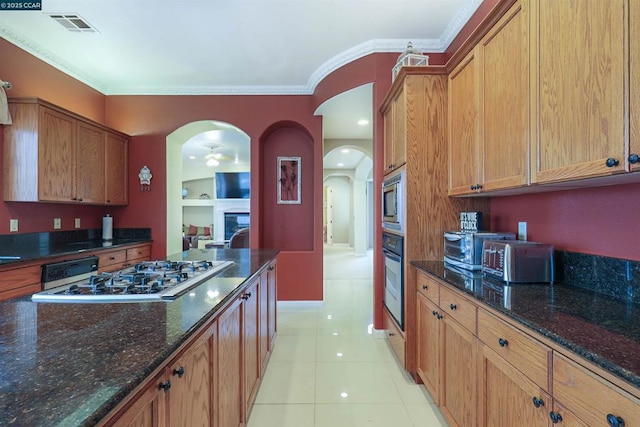 kitchen featuring crown molding, appliances with stainless steel finishes, light tile patterned floors, and dark stone counters