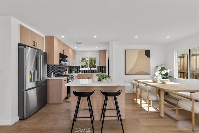 kitchen featuring a kitchen island, a breakfast bar area, breakfast area, stainless steel appliances, and light wood-type flooring