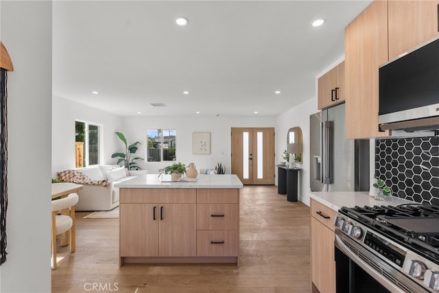 kitchen featuring light brown cabinetry, stainless steel appliances, french doors, and light wood-type flooring