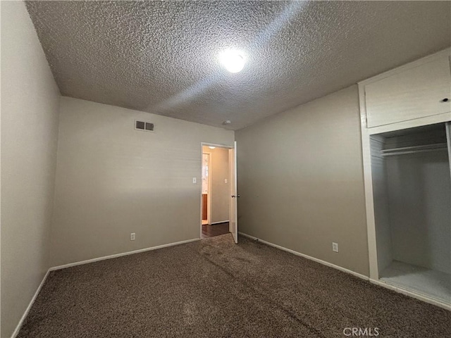 unfurnished bedroom with dark carpet, a textured ceiling, and a closet