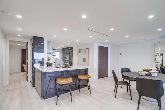 kitchen with light stone counters, light hardwood / wood-style floors, a breakfast bar, and a kitchen island