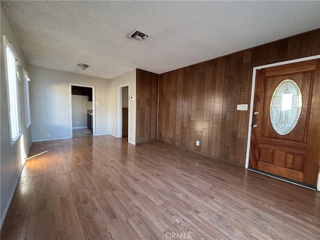 entrance foyer featuring wood-type flooring, a textured ceiling, and wood walls