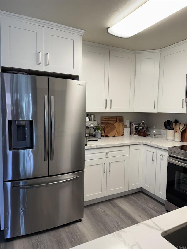 kitchen with light stone counters, appliances with stainless steel finishes, light wood-type flooring, and white cabinets