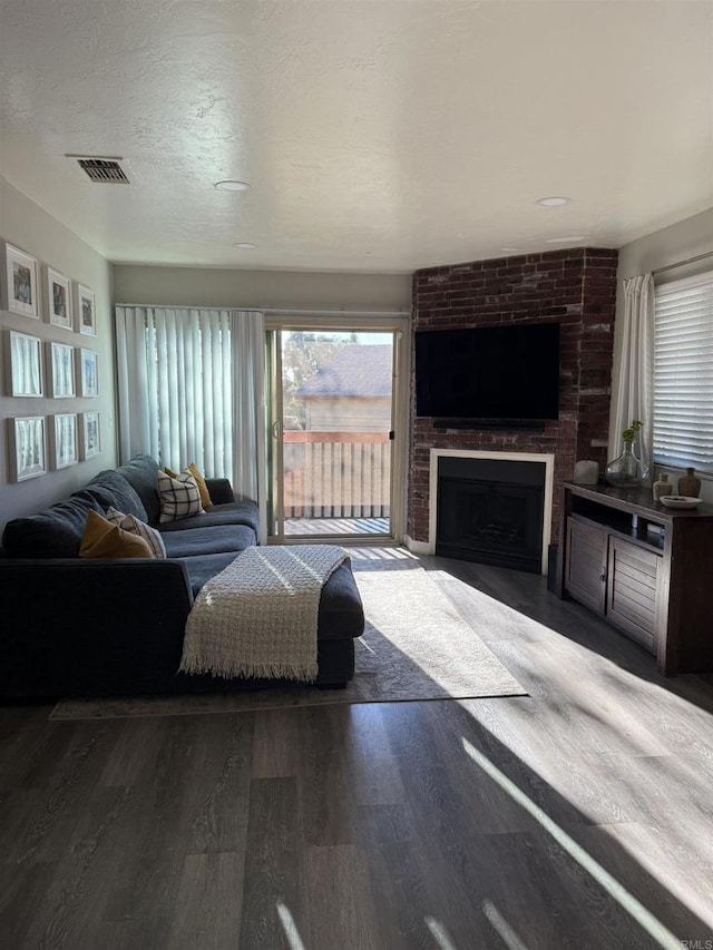 living room featuring dark wood-type flooring, a large fireplace, and a textured ceiling