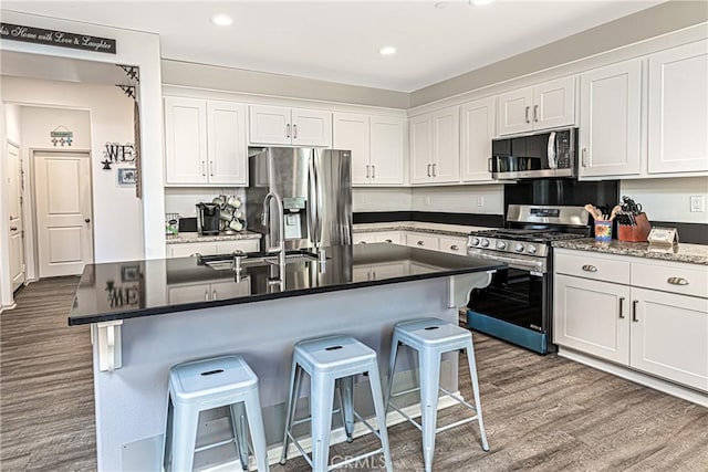 kitchen with stainless steel appliances, a kitchen breakfast bar, white cabinets, and a center island with sink