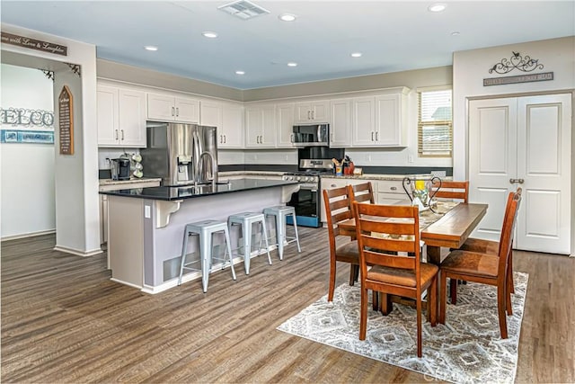 kitchen featuring a breakfast bar, appliances with stainless steel finishes, white cabinetry, a center island, and dark hardwood / wood-style flooring