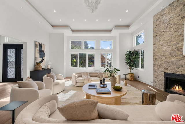 living room featuring a fireplace, a raised ceiling, a high ceiling, and light wood-type flooring