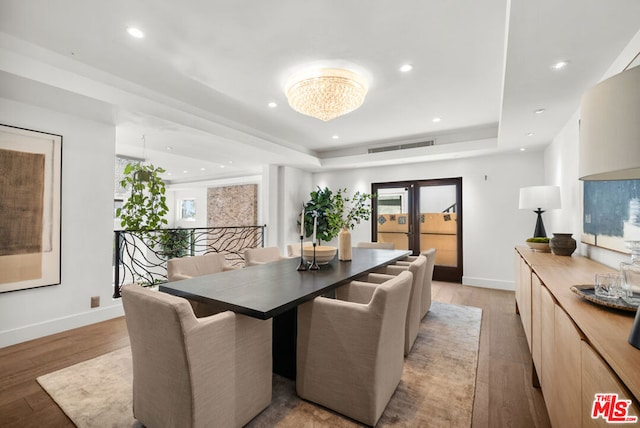 dining room with french doors, a notable chandelier, a raised ceiling, and light wood-type flooring