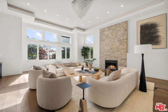 living room featuring a raised ceiling, wood-type flooring, a stone fireplace, and a high ceiling