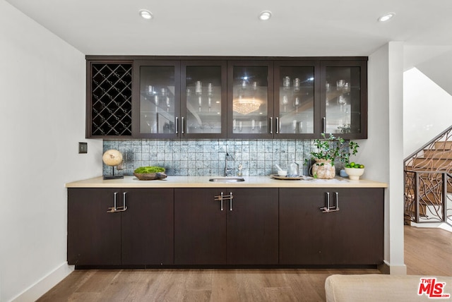 bar featuring dark brown cabinetry, sink, decorative backsplash, and light wood-type flooring