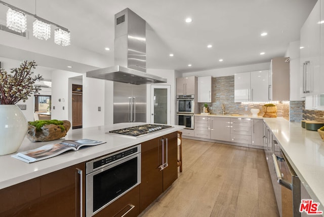 kitchen featuring white cabinetry, appliances with stainless steel finishes, island exhaust hood, light hardwood / wood-style floors, and backsplash