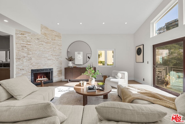 living room with sink, a stone fireplace, vaulted ceiling, and light wood-type flooring