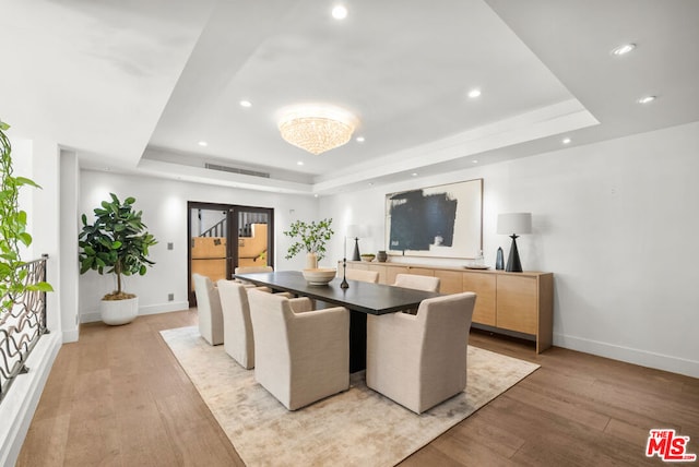 dining space featuring a raised ceiling, light wood-type flooring, and french doors