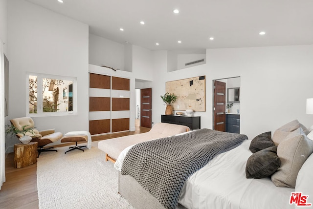 bedroom with high vaulted ceiling, ensuite bathroom, and light wood-type flooring