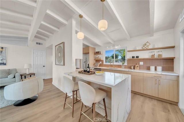 kitchen featuring lofted ceiling with beams, hanging light fixtures, a kitchen breakfast bar, kitchen peninsula, and light hardwood / wood-style floors