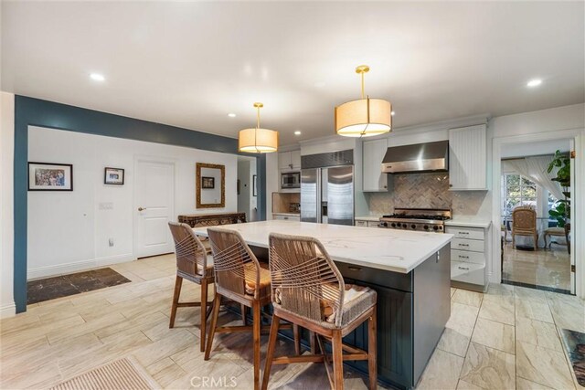 kitchen with gray cabinetry, built in appliances, a center island, pendant lighting, and wall chimney range hood