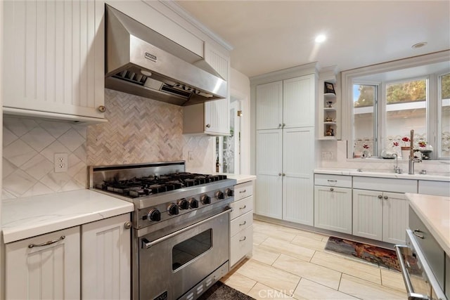 kitchen featuring sink, white cabinets, premium stove, and wall chimney exhaust hood